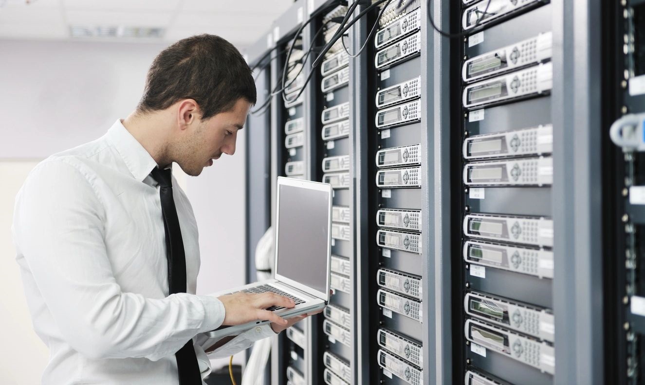A man holding a laptop and looking at servers